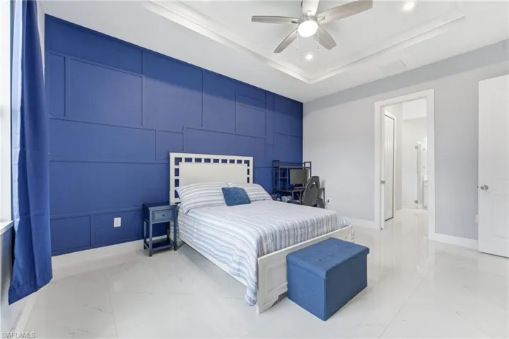 Bedroom featuring a raised ceiling, an accent wall, a decorative wall, light marble finish floors, and ceiling fan