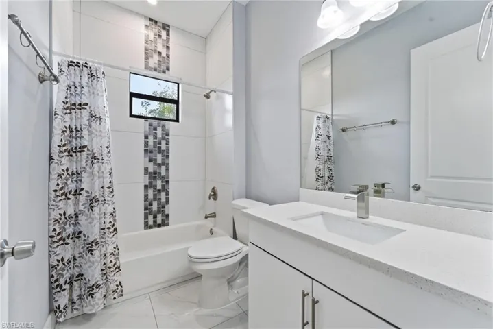 Bathroom with vanity, shower / tub combo, and light marble finish flooring