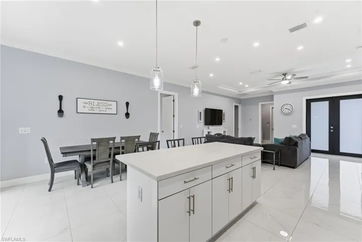 Kitchen with pendant lighting, a kitchen island, white cabinets, light stone countertops, and ceiling fan