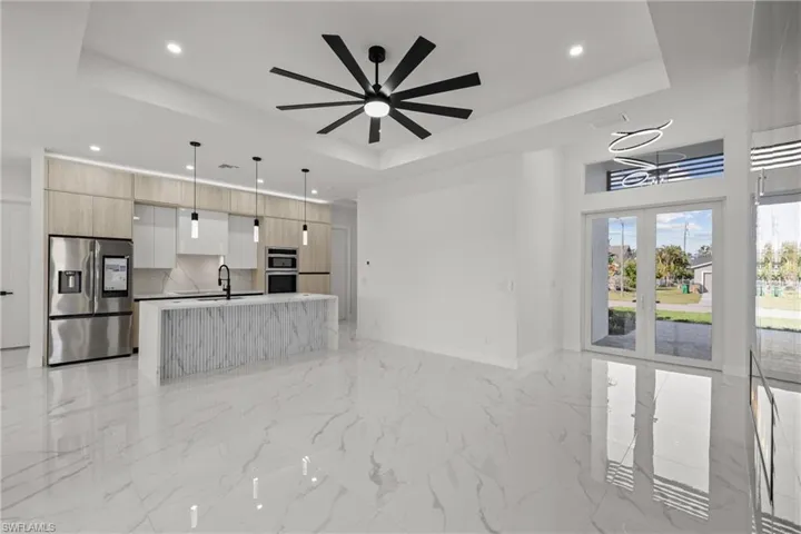 Unfurnished living room featuring a tray ceiling, recessed lighting, a ceiling fan, light marble finish flooring, and a sink