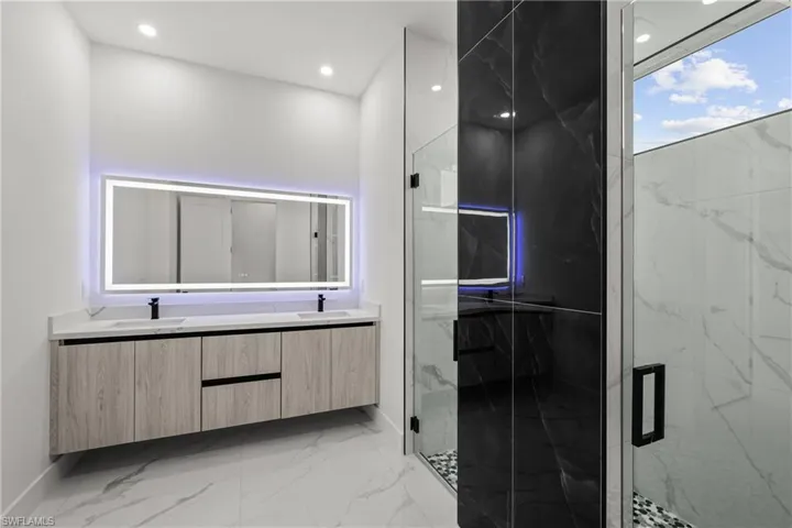 Full bath with double vanity, a marble finish shower, baseboards, marble finish flooring, and recessed lighting