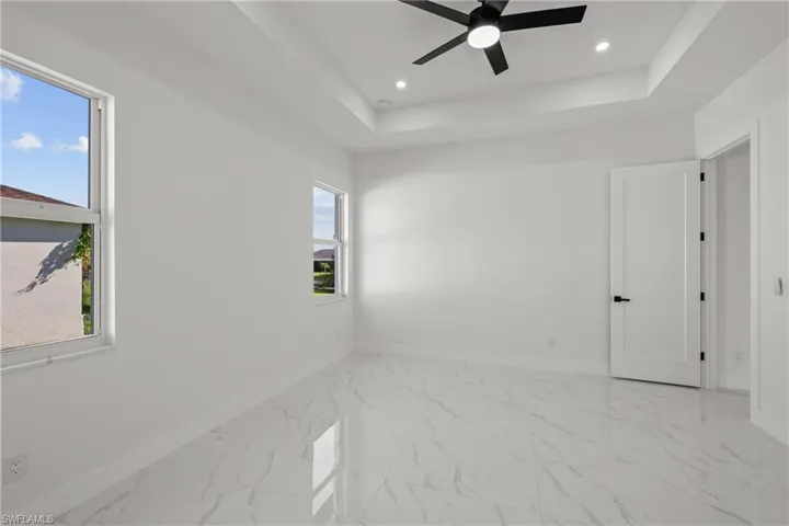 Empty room with baseboards, a ceiling fan, light marble finish floors, recessed lighting, and a raised ceiling