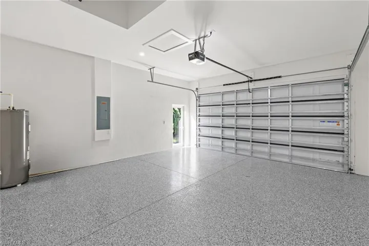 Garage with electric water heater, electric panel, and a garage door opener
