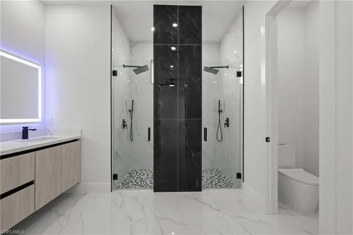 Full bathroom featuring toilet, marble finish flooring, a marble finish shower, vanity, and baseboards