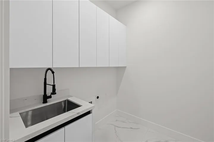 Clothes washing area with cabinet space, light marble finish floors, baseboards, and electric dryer hookup