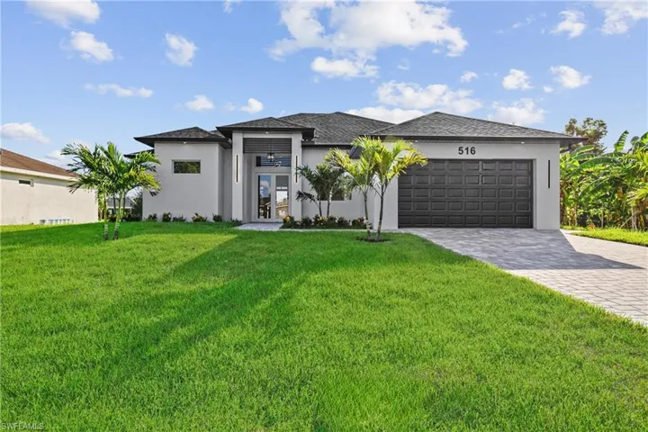 Prairie-style home with stucco siding, an attached garage, a front lawn, and decorative driveway