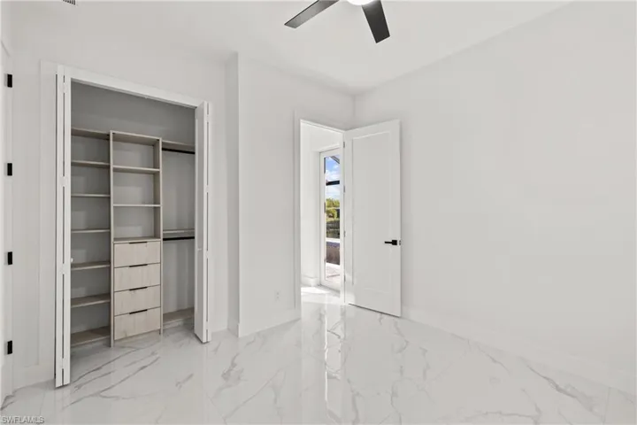 Unfurnished bedroom featuring light marble finish floors, baseboards, a ceiling fan, and a closet