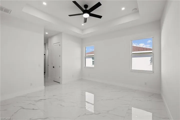Empty room with a raised ceiling, recessed lighting, baseboards, ceiling fan, and light marble finish floors