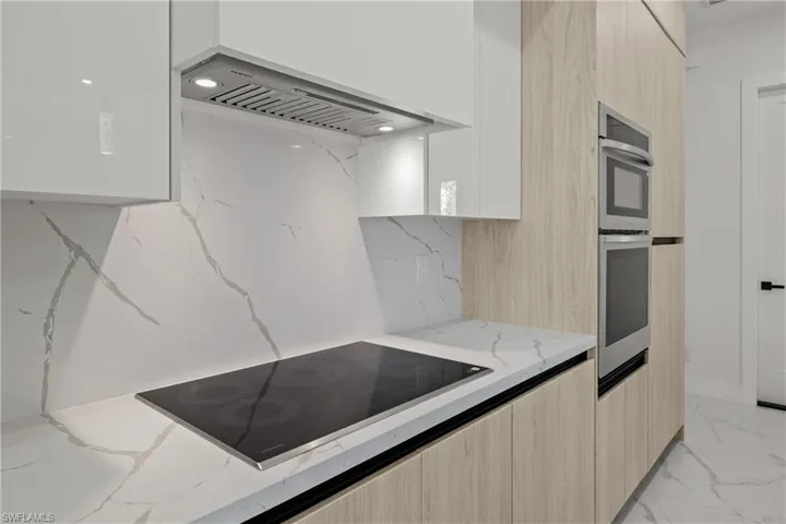 Kitchen with modern cabinets, black electric stovetop, custom range hood, and light stone countertops