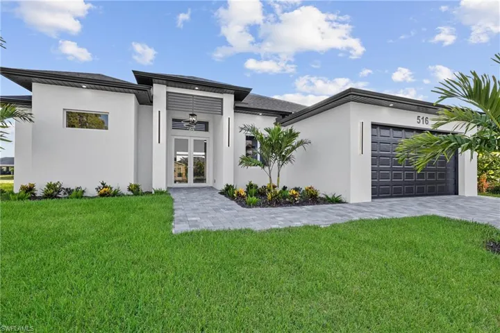View of front of house featuring french doors, an attached garage, a front yard, stucco siding, and decorative driveway