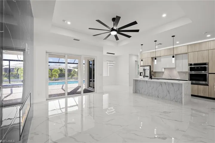 Unfurnished living room with a raised ceiling, a ceiling fan, light marble finish floors, recessed lighting, and a sink