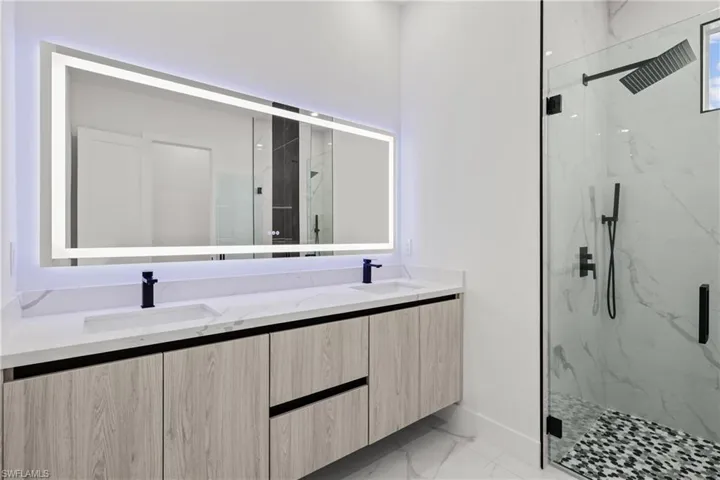 Full bathroom featuring marble look tiles, a marble finish shower, double vanity, and baseboards