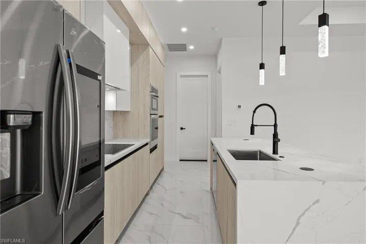 Kitchen with modern cabinets, stainless steel refrigerator with ice dispenser, a sink, light brown cabinetry, and recessed lighting