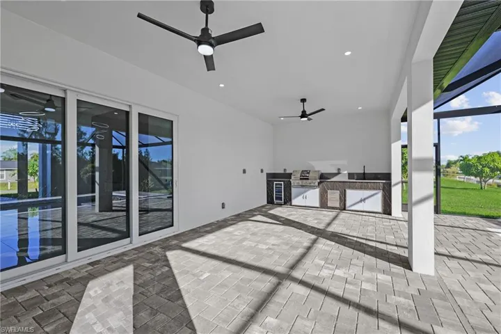 View of patio with an outdoor kitchen, a ceiling fan, grilling area, and glass enclosure