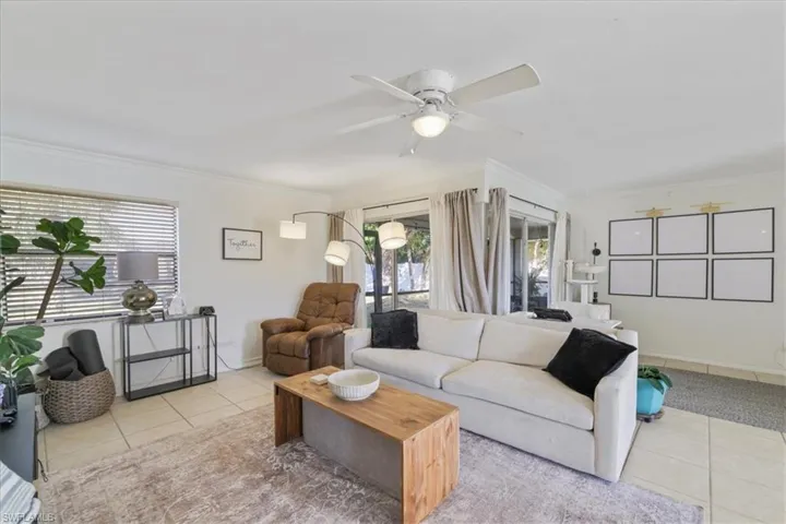 Living room with light tile patterned floors, crown molding, and ceiling fan