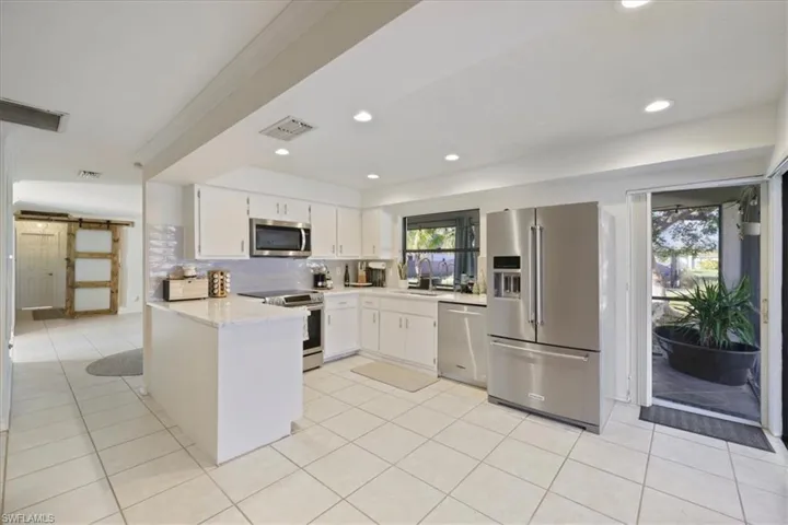 Kitchen with appliances with stainless steel finishes, a peninsula, white cabinets, and light tile patterned flooring