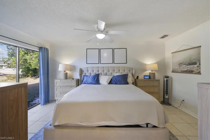 Tiled bedroom with access to outside, a textured ceiling, ornamental molding, and ceiling fan