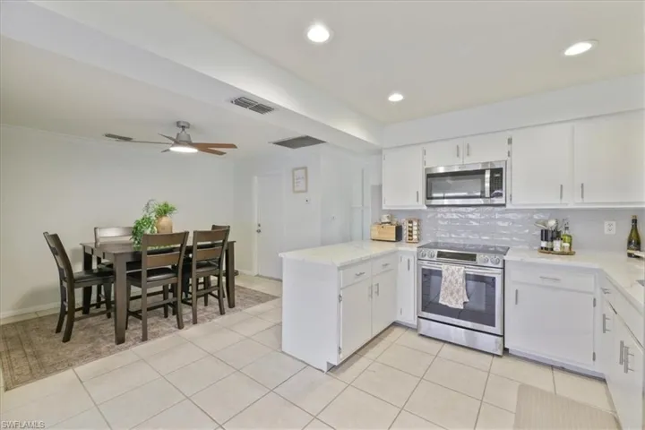 Kitchen with a peninsula, stainless steel appliances, white cabinetry, decorative backsplash, and light stone counters