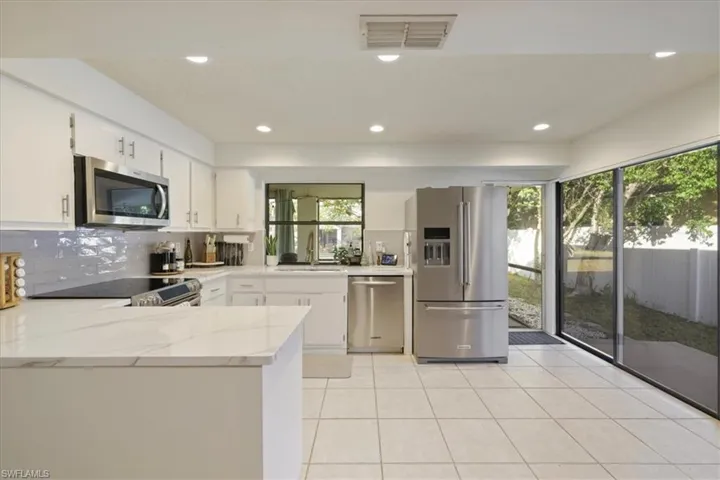Kitchen with appliances with stainless steel finishes, a peninsula, light stone counters, white cabinetry, and recessed lighting