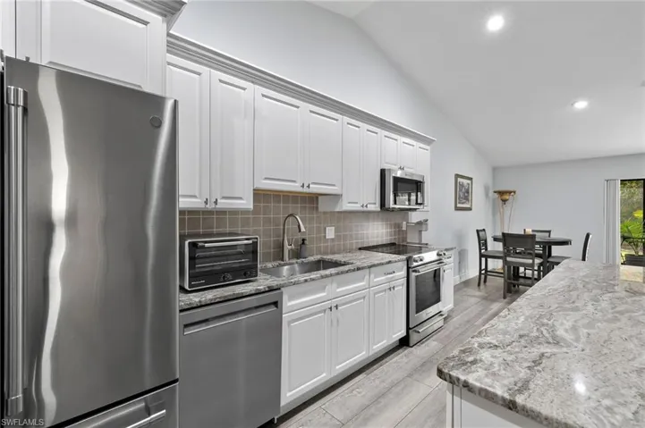Kitchen featuring white cabinetry, stainless steel appliances, light wood-type flooring, lofted ceiling, and backsplash