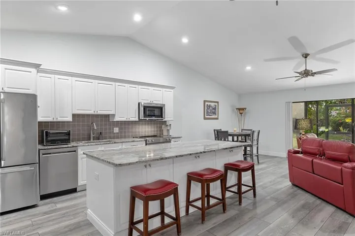 Kitchen featuring white cabinets, backsplash, vaulted ceiling, and appliances with stainless steel finishes