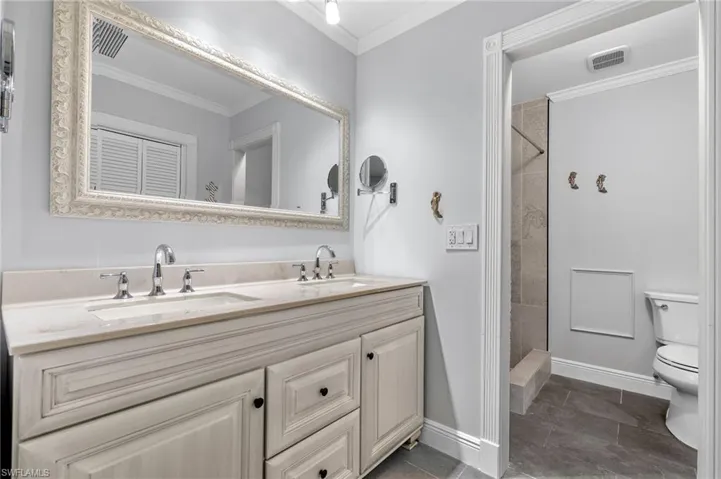 Bathroom featuring tiled shower, crown molding, dual vanity, toilet, and tile patterned flooring