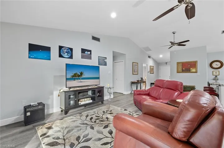 Living room featuring ceiling fan, wood-type flooring, and vaulted ceiling