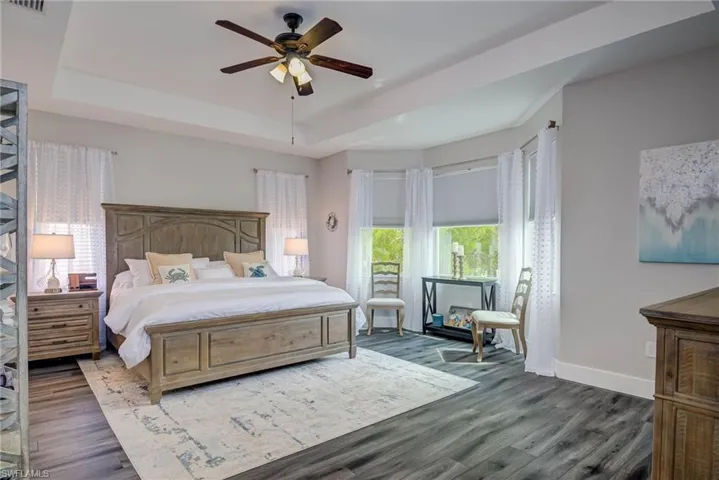 Bedroom featuring a ceiling fan, dark wood-style flooring, baseboards, and a tray ceiling