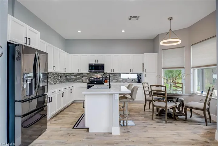 Kitchen with appliances with stainless steel finishes, light countertops, white cabinets, a kitchen bar, and visible vents