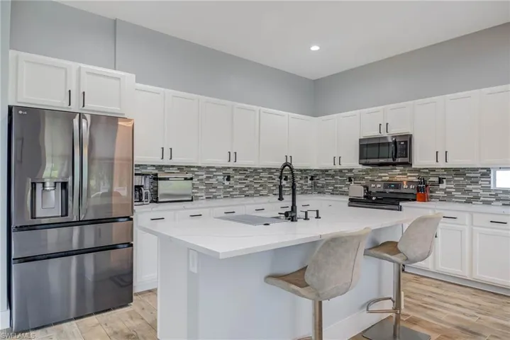 Kitchen featuring white cabinetry, stainless steel appliances, light wood finished floors, and decorative backsplash