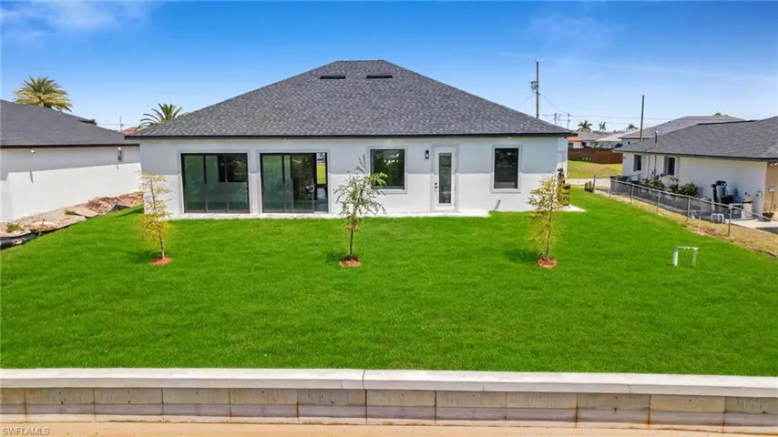 Rear view of house with stucco siding, roof with shingles, fence, and a lawn