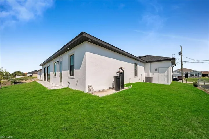 Rear view of house with a yard, central AC unit, and stucco siding