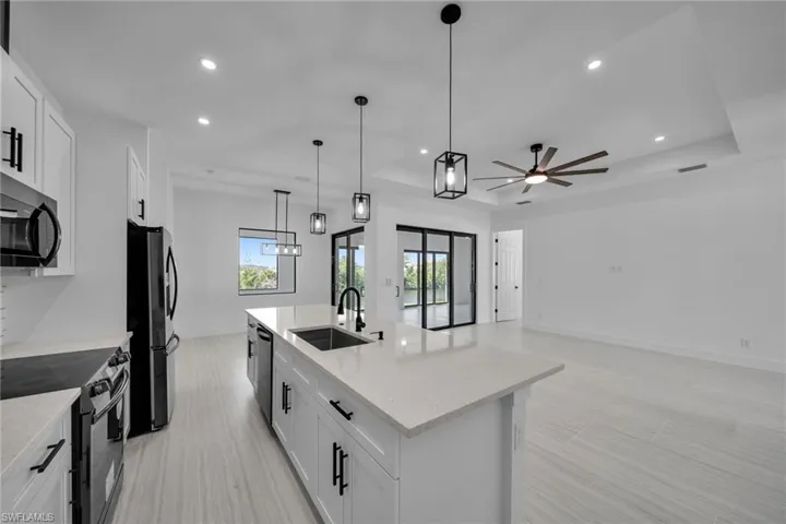 Kitchen with a sink, freestanding refrigerator, black microwave, stainless steel electric range oven, and a ceiling fan