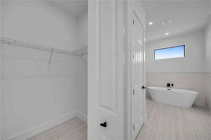 Bathroom featuring baseboards, recessed lighting, a spacious closet, and a freestanding bath