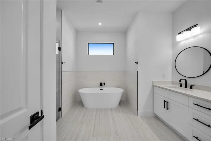 Full bathroom with a soaking tub, tile walls, visible vents, and vanity