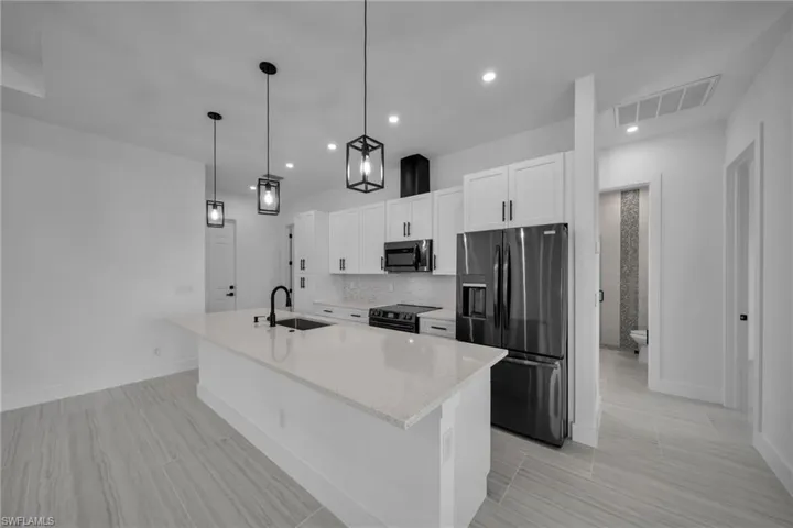Kitchen with stainless steel microwave, a sink, black refrigerator with ice dispenser, visible vents, and electric range oven