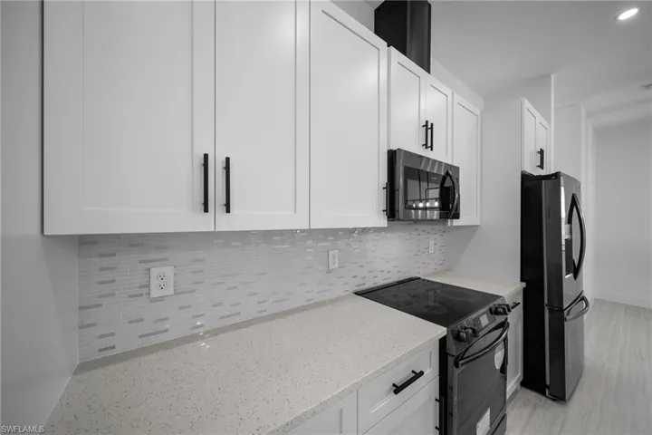 Kitchen featuring stainless steel microwave, freestanding refrigerator, light stone counters, black range with electric stovetop, and white cabinets
