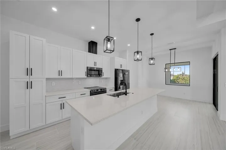 Kitchen featuring a sink, a center island with sink, black fridge, decorative backsplash, and white cabinets