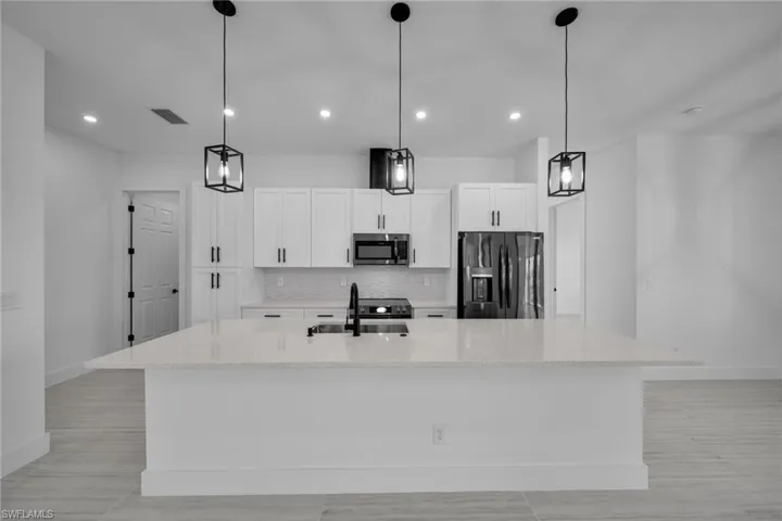 Kitchen with a sink, visible vents, stainless steel microwave, baseboards, and black refrigerator with ice dispenser