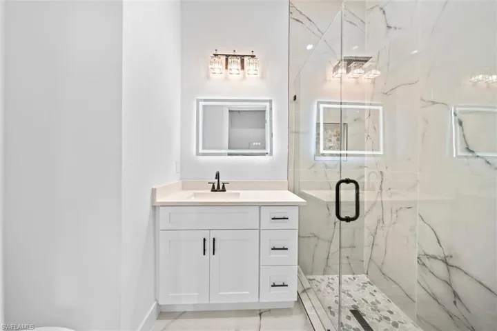 White vanity with a light-toned countertop and an illuminated mirror