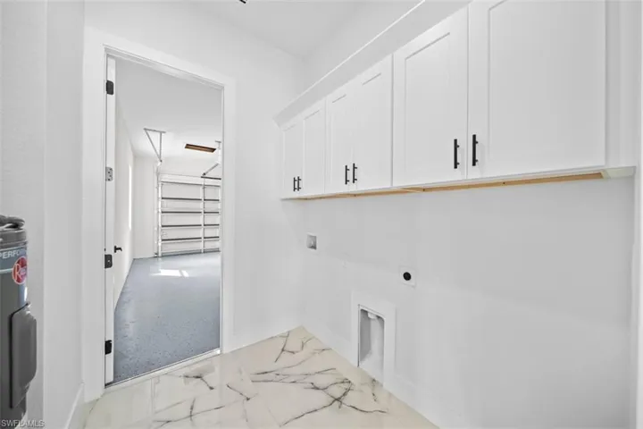White shaker-style cabinetry with black hardware, marbling-patterned floor tiling, and a separate utility area