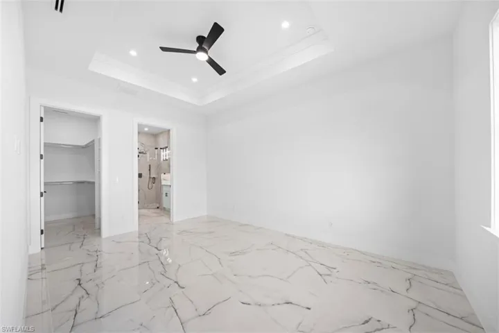 Tray ceiling with crown molding, recessed lighting, ceiling fan, large format marble-look tile flooring, and an open closet