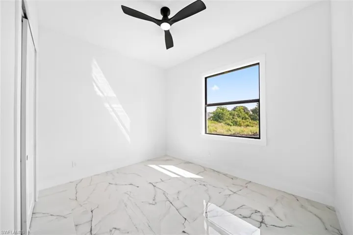 White walls, a ceiling fan with black blades, and a single window with a black frame