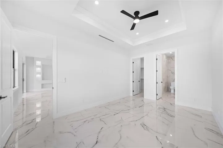 White marble-look flooring, recessed lighting, tray ceiling, and a black ceiling fan