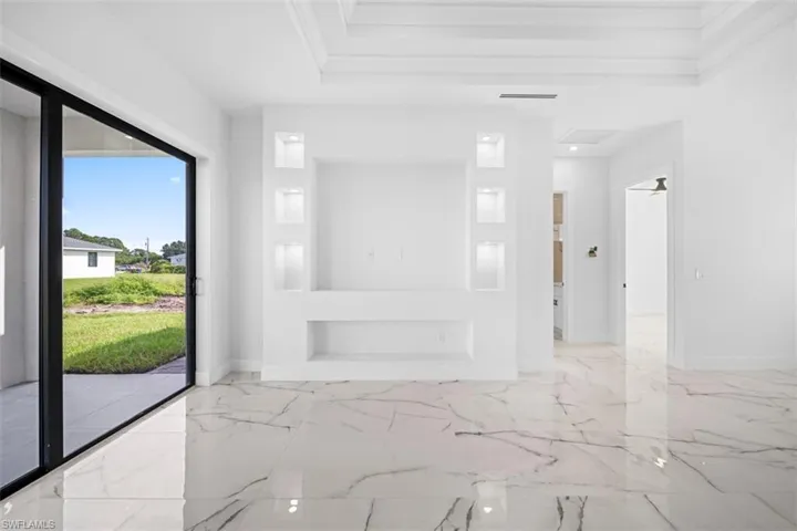 Sliding glass doors opening to the exterior, built-in display niches with recessed lighting, tray ceiling, and polished marble-look tile flooring