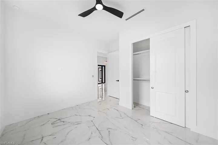 White walls with a black ceiling fan, large format tile flooring, and a sliding closet door