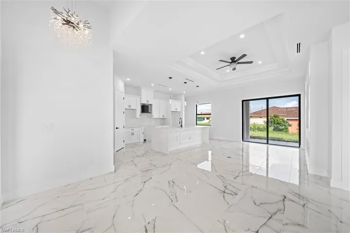 Open-concept interior featuring large-format tile flooring, a contemporary chandelier, a kitchen island with seating, a coffered ceiling with recessed lighting and ceiling fan, and sliding glass doors
