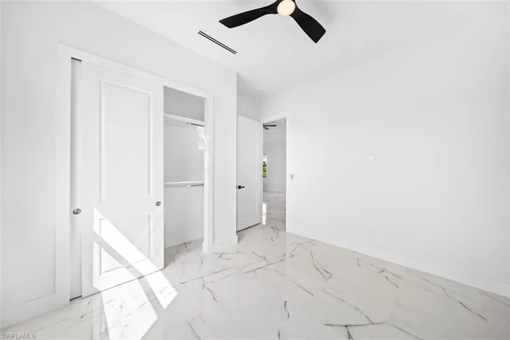 Expansive white tile flooring with dark veining, modern ceiling fan, white wall finishes, and a built-in closet with sliding panel doors