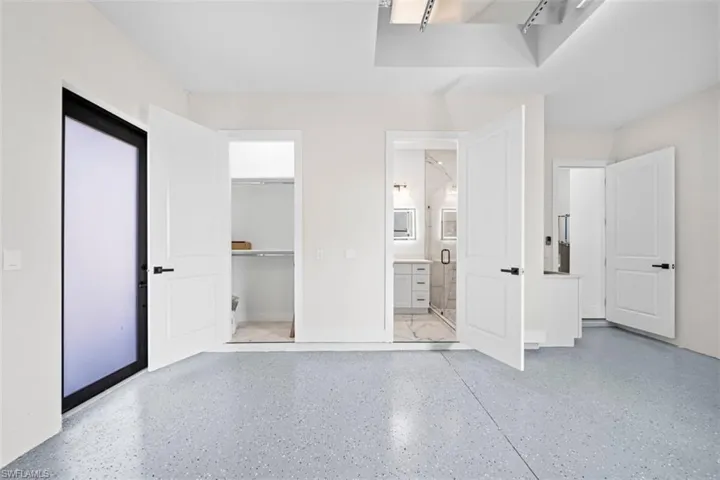 Epoxy flooring, white paneled doors, built-in shelving, white floating vanity, and a glass-enclosed shower