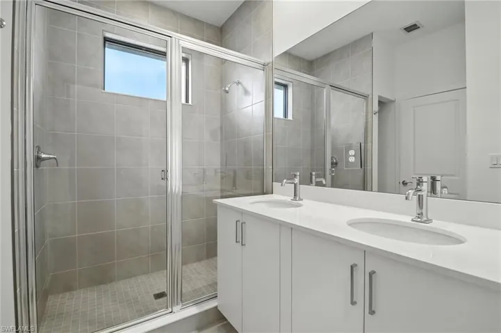 Full bath with double vanity, plenty of natural light, and a stall shower